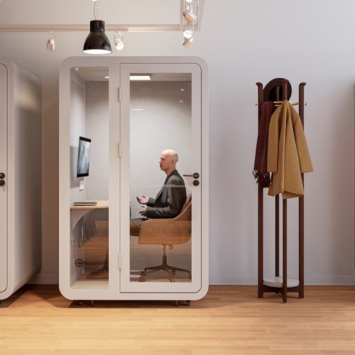 Person in a soundproof Solo Plus Booth, using a laptop for a video conference in an office.